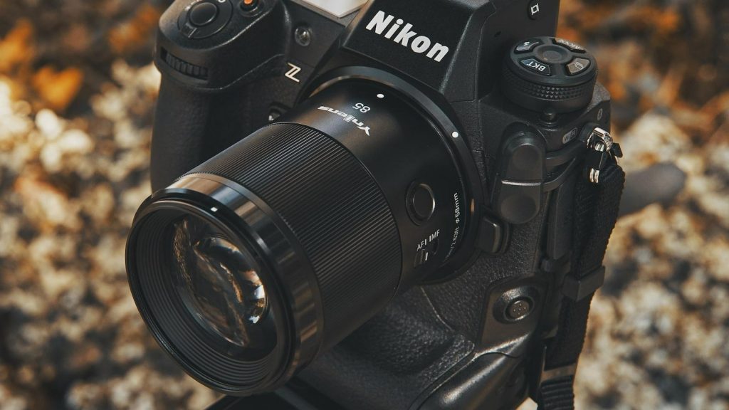 Компактний об'єктив Yongnuo YN 85mm f/1.8Z DF DSM з кнопкою Fn та перемикачем AF/MF на камері Nikon Z на фоні осіннього листя
