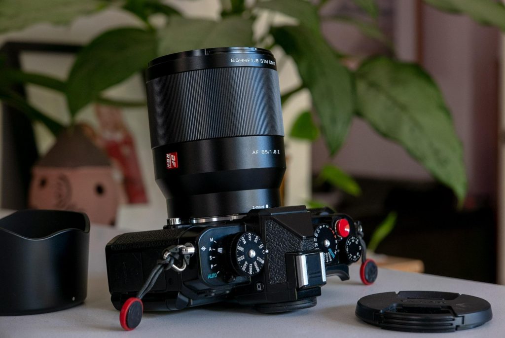 Об'єктив Viltrox AF 85mm f/1.8 II Z з маркуванням DF RBW на камері Nikon Zf поруч зі знятою пелюстковою блендою на столі біля рослин